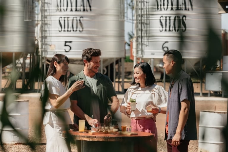 Vier Freunde, die im Hoochery Distillery Café, Kununurra, Westaustralien, im Freien um einen Tisch herum stehen und Drinks genießen, im Hintergrund Silos © Tourism Western Australia Vier Freunde, die im Hoochery Distillery Café, Kununurra, Westaustralien, im Freien um einen Tisch herum stehen und Drinks genießen, im Hintergrund Silos © Tourism Western Australia