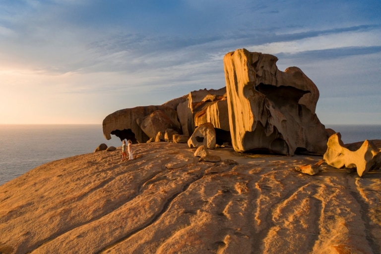 Two people walking besides the large formations of the Remarkable Rocks during sunset with the ocean behind on Kangaroo Island, South Australia © South Australian Tourism Commission Two people walking besides the large formations of the Remarkable Rocks during sunset with the ocean behind on Kangaroo Island, South Australia © South Australian Tourism Commission