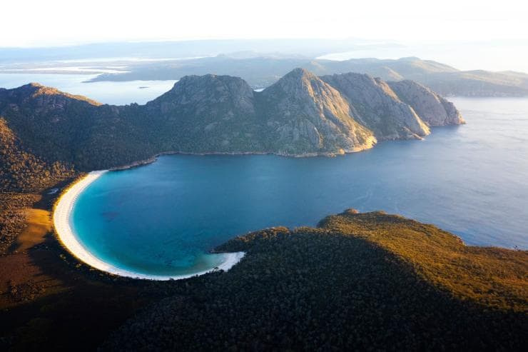 Vista aerea di Wineglass Bay e delle montagne circostanti coperte di alberi al Freycinet National Park, Tasmania © Lauren Bath