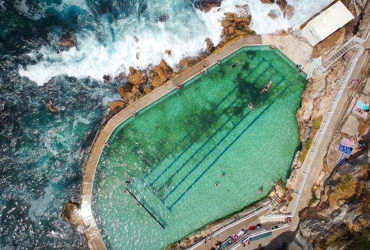 Luftaufnahme von Menschen, die in den Bronte Baths schwimmen, während die Wellen des Ozeans gegen ihren Rand schlagen, Bronte Beach, Sydney, New South Wales © Ashlea Wheeler