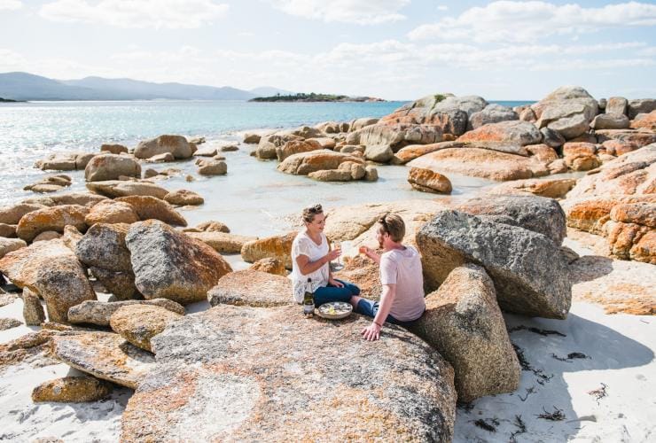 A couple enjoys a picnic on the rocks near Waubs Bay Beach, Bicheno, Tasmania © Stu Gibson