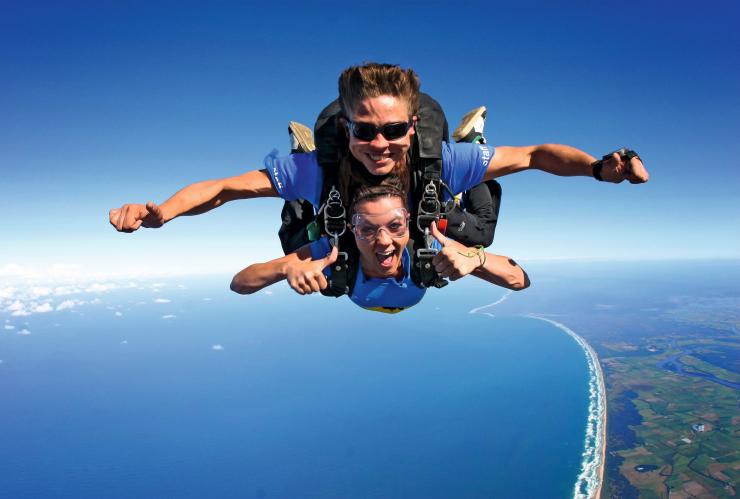 Two people smiling while tandem skydiving above a lush green coastline with Skydive Australia, Cairns, Queensland © Skydive Australia