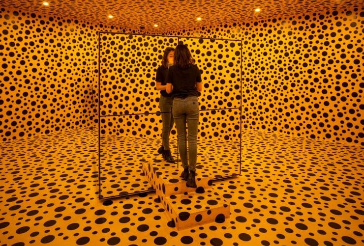 A woman stands in a room completely covered in orange with black dots at the National Gallery of Australia, Canberra, Australian Capital Territory © Tourism Australia