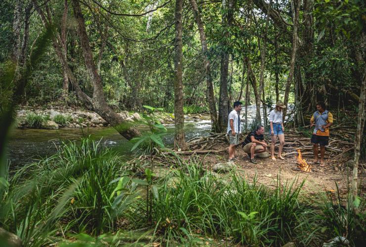 A group of people and a guide gathered around a fire beside a river in a rainforest with Walkabout Cultural Adventures, Port Douglas, Tropical North Queensland © Tourism and Events Queensland