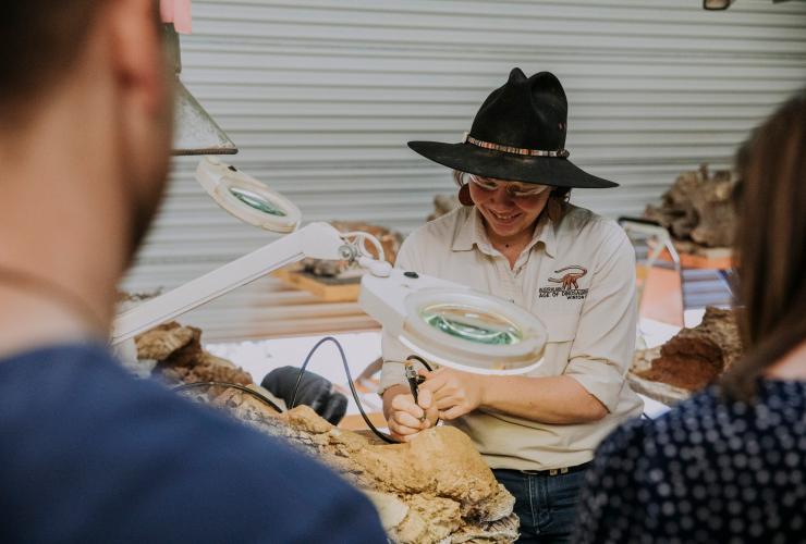 A museum worker carefully uncovering fossils under a magnifying glass at the Australian Age of Dinosaurs museum, Winton, Queensland © Tourism and Events Queensland