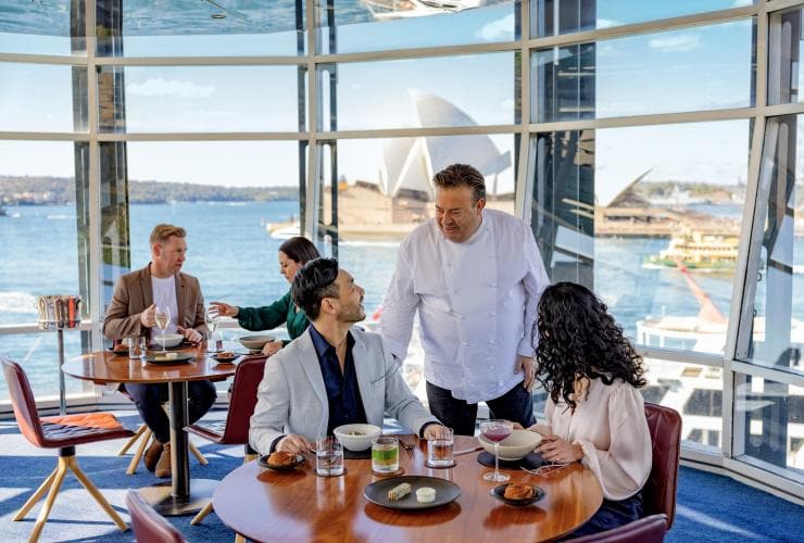 Chef Peter Gilmore chatting with a couple seated at a table overlooking Sydney Harbour at Quay Restaurant, Sydney, New South Wales © Tourism Australia
