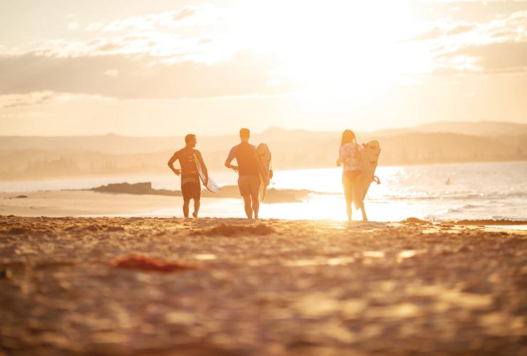 Three friends running across sand towards the ocean holding surfboards as the sun rises beyond, Snapper Rocks, Gold Coast, Queensland © Tourism and Events Queensland