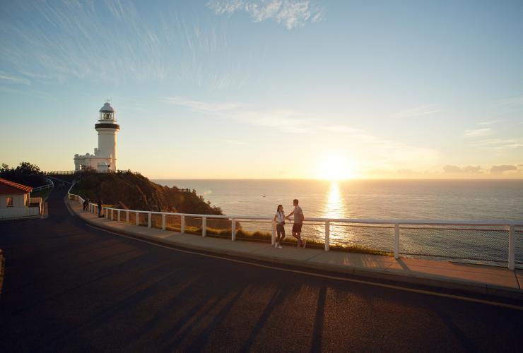 A couple leaning against a railing overlooking the ocean during sunrise with the Cape Byron Lighthouse to their left, Byron Bay, New South Wales © Hugh Stewart/Destination NSW