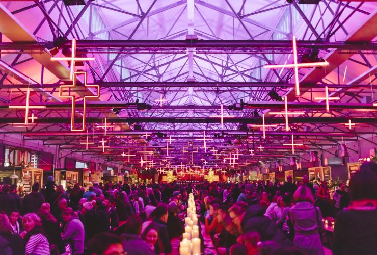 A room filled with people seated at long tables beneath purple and orange lights during Dark Mofo Winter Feast, Hobart, Tasmania © Tourism Tasmania