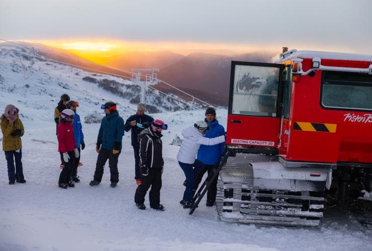 A group of people standing on top of a snowy mountain during a bright golden sunrise at Sunrise Sessions, Thredbo, New South Wales © Thredbo