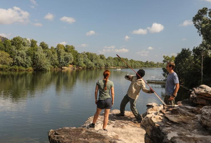 Des touristes accompagnés d'un guide membre des peuples aborigènes d'Australie jetant une lance depuis le bord d'une rivière lors d'une croisière Guluyambi Cultural Cruise, Kakadu National Park, Territoire du Nord © Tourism NT/James Fisher