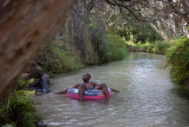 Un homme flottant sur les eaux claires d'Eli Creek, installé dans une bouée gonflable, admirant les arbres qui défilent au-dessus de lui à K'gari, Queensland © Tourism and Events Queensland