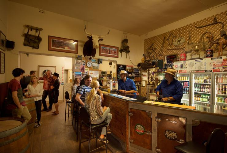 Dua bartender bertopi koboi menyajikan bir ke sekelompok pengunjung di bar yang unik di Marree Hotel, Flinders Ranges & Outback, South Australia © South Australian Tourism Commission