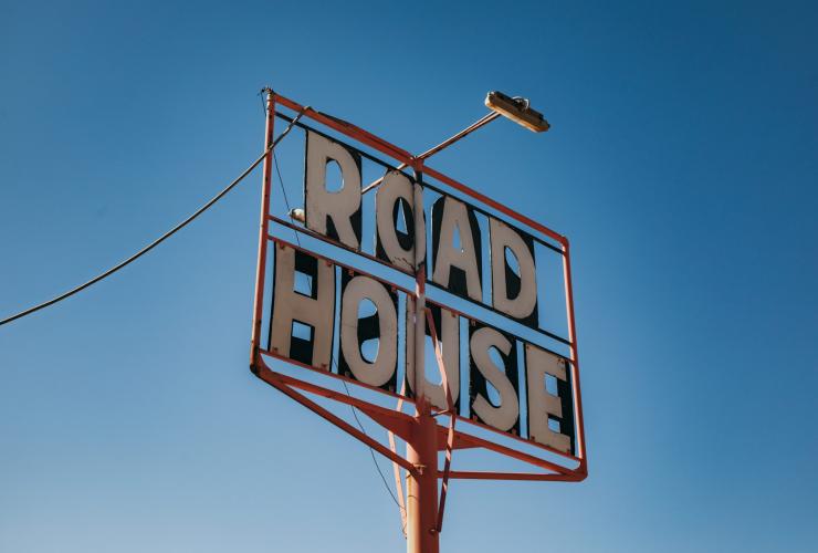 Plang bertuliskan "Road House" yang dipotret dari sudut bawah dengan latar belakang langit biru cerah di Pink Roadhouse, Flinders Ranges & Outback, South Australia © South Australian Tourism Commission