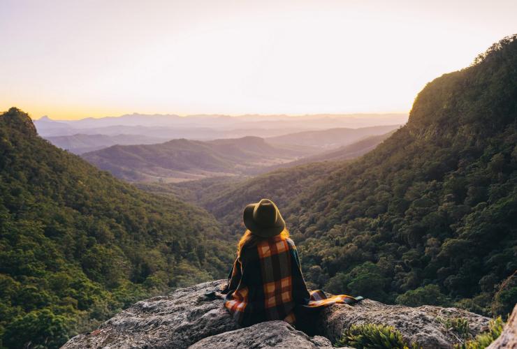 Seseorang duduk di atas puncak di Lamington National Park dengan pemandangan pegunungan yang diselimuti pepohonan di Queensland © Tourism and Events Queensland