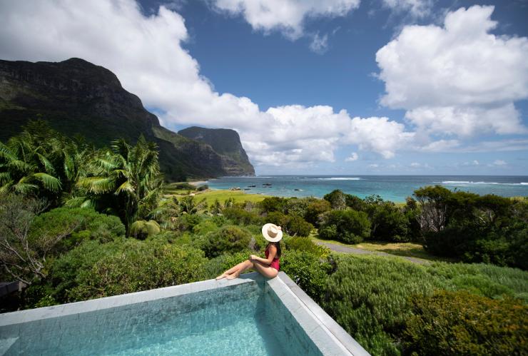 Seorang wanita sedang duduk di tepi kolam Capella Lodge melihat pemandangan rimbun dan pesisir pantai Lord Howe Island, New South Wales © Tom Archer