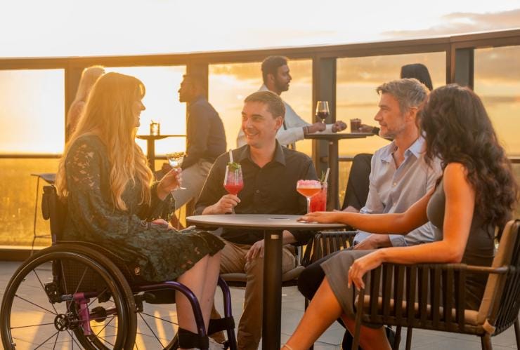 Un gruppo di amici, tra cui una persona in sedia a rotelle, che bevono un drink al Sol Rooftop, Adelaide, South Australia © Tourism Australia