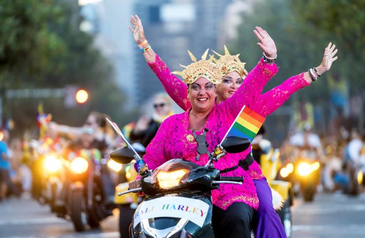 Due persone su una moto con vestiti color rosa acceso che salutano guardando la fotocamera al Sydney Gay and Lesbian Mardi Gras, Sydney, New South Wales © Jeffrey Feng