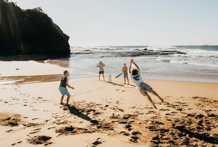 Quattro amici che giocano a cricket sulla sabbia a Coledale Beach, Thirroul, New South Wales © Destination NSW