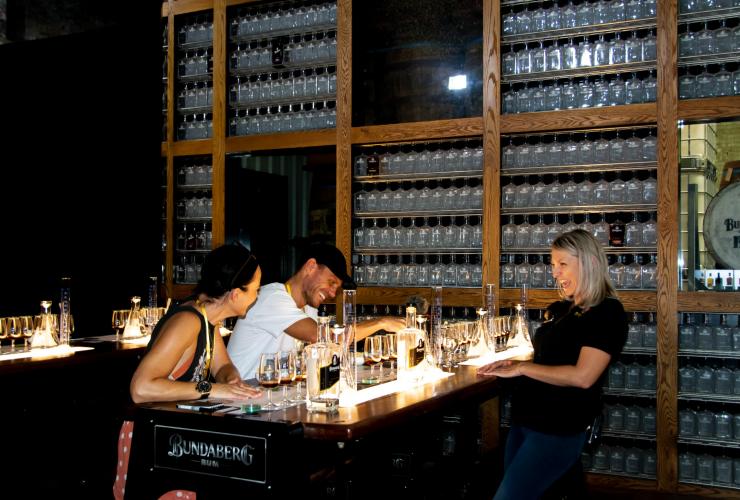 Tre persone che ridono intorno a un tavolo pieno di bicchieri con rum durante la Bundaberg Rum Experience, Bundaberg, Queensland © Tourism and Events Queensland