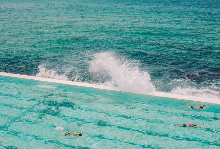 Persone che nuotano nelle limpide acque blu della piscina di Bondi Icebergs con le onde dell'oceano che si infrangono ai lati a Bondi, New South Wales © Tourism Australia