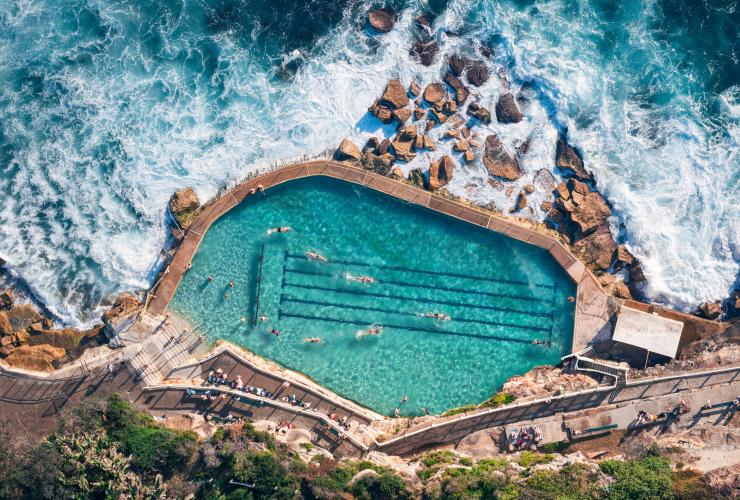 Vista aerea di persone che nuotano nelle acque turchesi di Bronte Baths, con le onde dell'oceano che si infrangono contro le rocce intorno alla piscina, Bronte Beach, Sydney, New South Wales © Tourism Australia