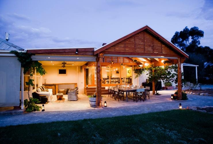 Esterno di una tenuta di sera, con lanterne disseminate sul pavimento, un'accogliente area lounge all'aperto e una grande tavola apparecchiata nel patio presso l'Arkaba Station, Flinders Ranges, South Australia © Wild Bush Luxury