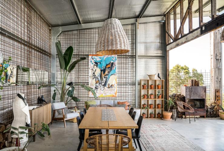 Una grande stanza aperta con un tavolo da pranzo, opere d'arte, piante in vaso e una parete completamente aperta che lascia entrare la luce del sole presso Blackbird, Byron Bay, New South Wales © Blackbird/Saul Goodwin @propertyshotphotography