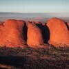 ノーザンテリトリー、ウルル - カタ・ジュタ国立公園にて、広々としたアウトバックの地平線からそそり立つ巨大な赤い一枚岩 © Tourism Australia