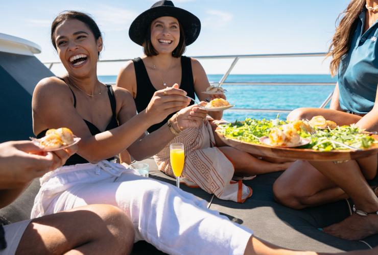 在西澳州的羅特尼斯島，幾個滿面笑容的朋友一起在Rottnest Cruises的遊船上享用一盤海鮮©澳洲旅遊局
