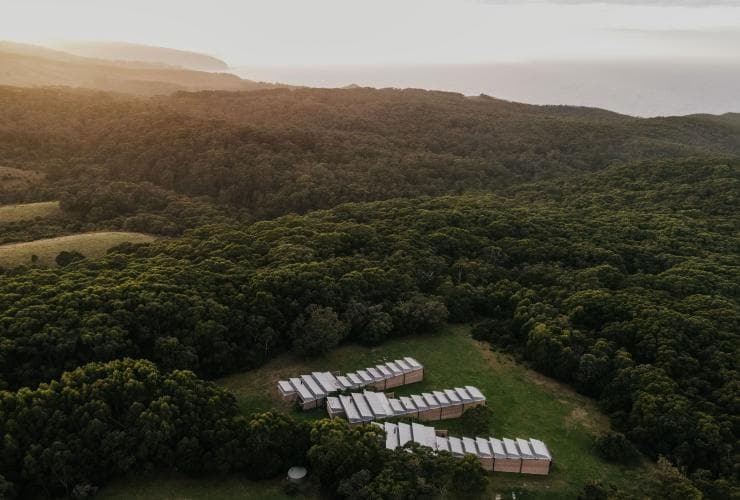 維多利亞州沃特山（Wattle Hill）艾基拉小屋的高空景致，三排小型建築周圍是草木，遠處可見海洋©艾基拉小屋